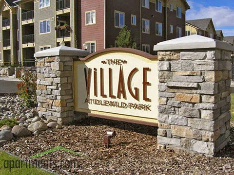 A sign for The Village at Wildwood Park in front of apartment buildings.