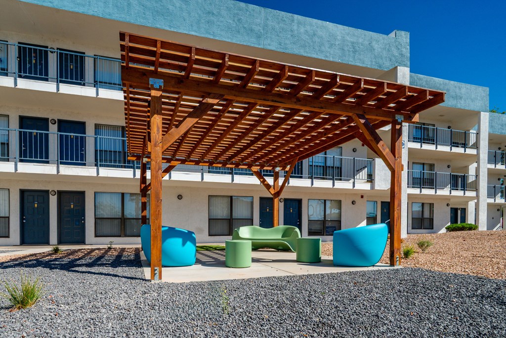 A wooden pergola is in front of a building with blue doors.