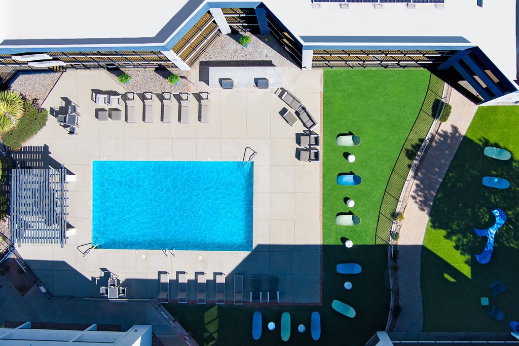 A large swimming pool is surrounded by a grassy area and a building.