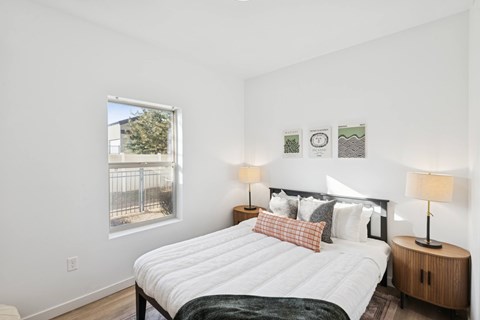 A bedroom with a large bed and a window overlooking a fence.