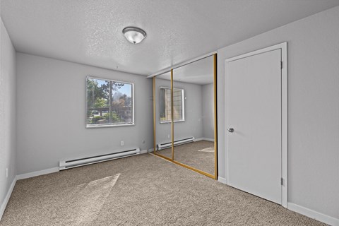 A bedroom with a carpeted floor and a large mirror on the wall.