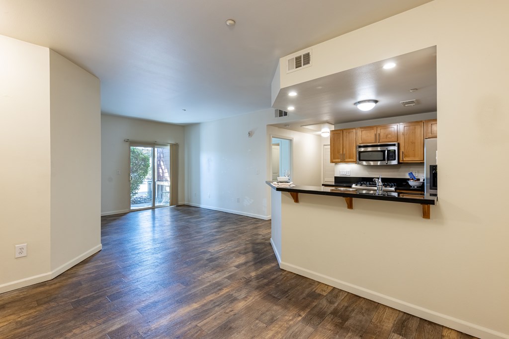 A spacious living room with hardwood floors and a kitchenette in the background.