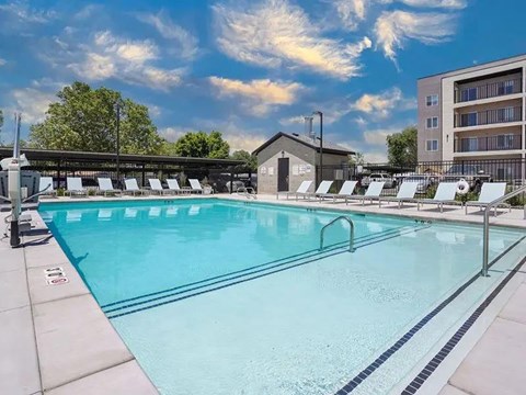 A large outdoor swimming pool with sun loungers and a building in the background.