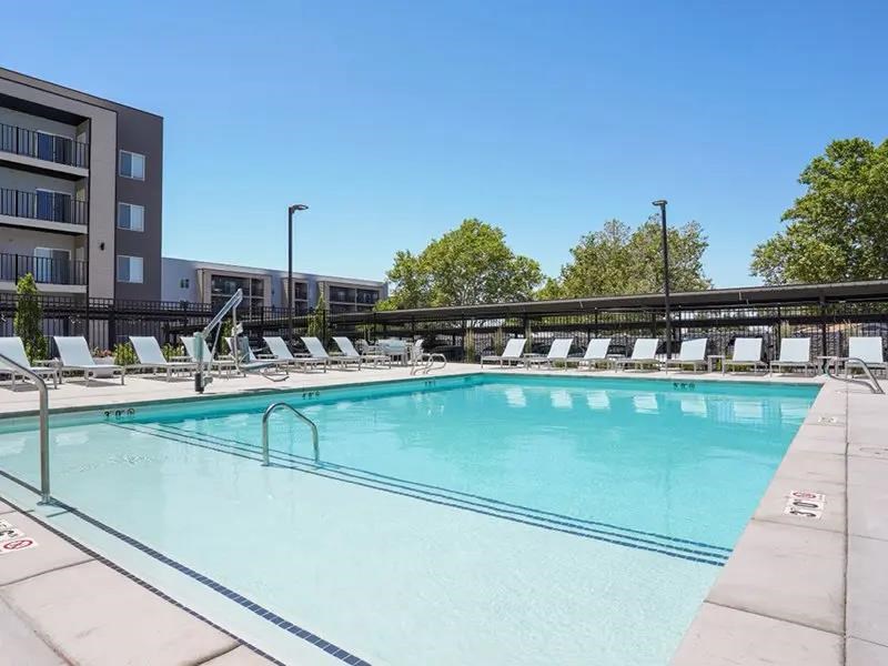 A large swimming pool with lounge chairs and apartment buildings in the background.