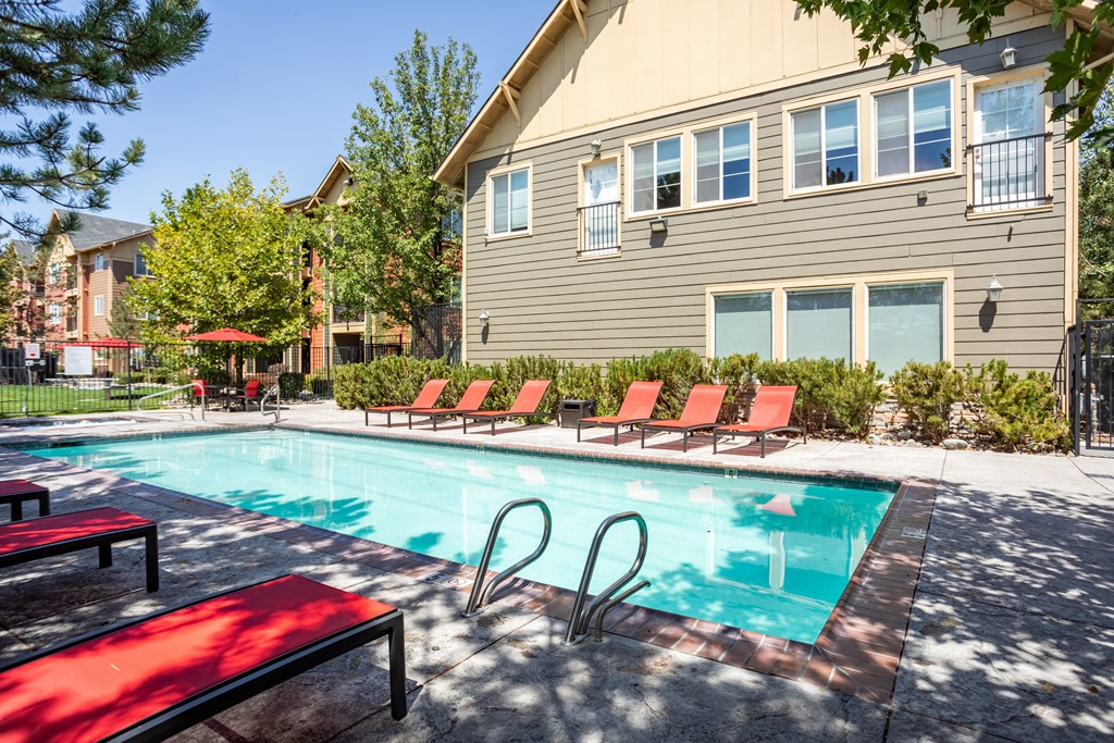 A pool with red chairs and a bench in front of a building.
