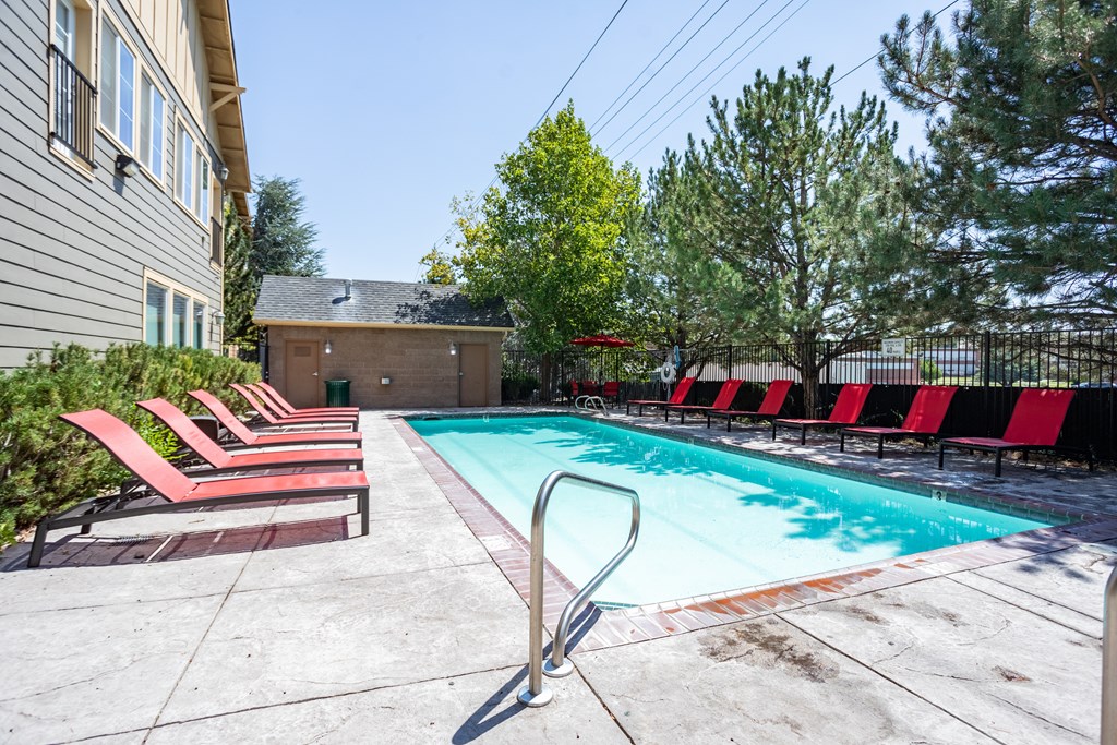 A pool with red chairs and a building in the background.