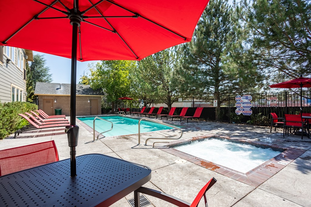 A red umbrella is shading a table in a poolside area.
