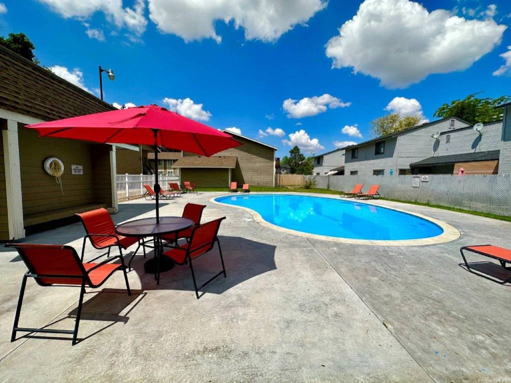 A pool area with a table and chairs and a red umbrella.