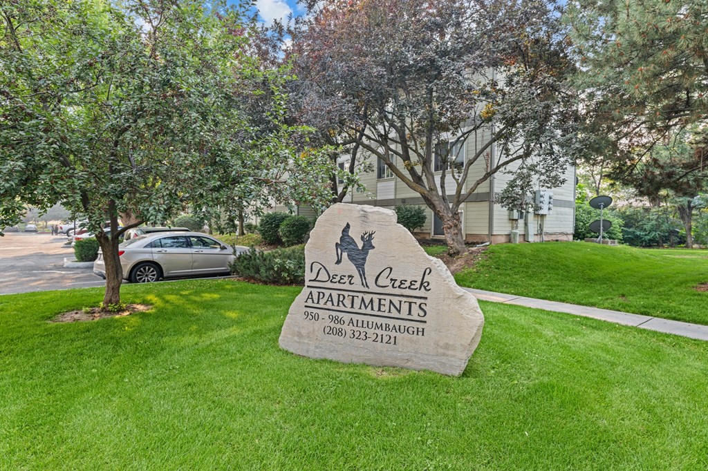 A sign for Deer Creek Apartments is in the foreground of a grassy area.