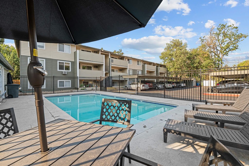 A pool surrounded by wooden deck chairs and umbrellas.