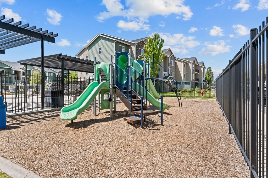 A playground with a green slide and a brown ground.