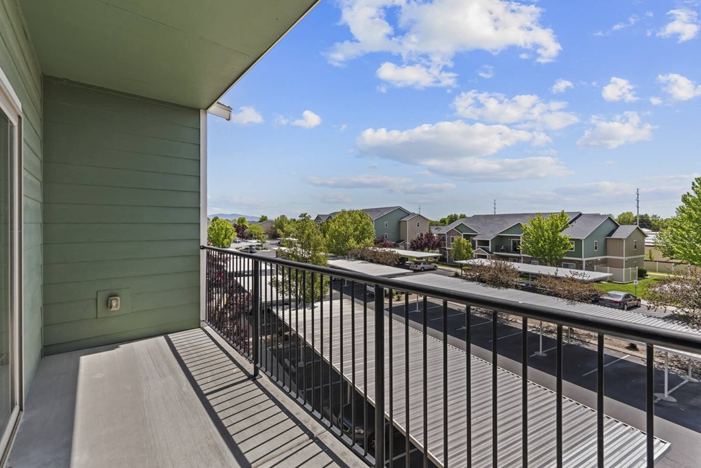A balcony with a metal railing overlooks a street with cars and houses.