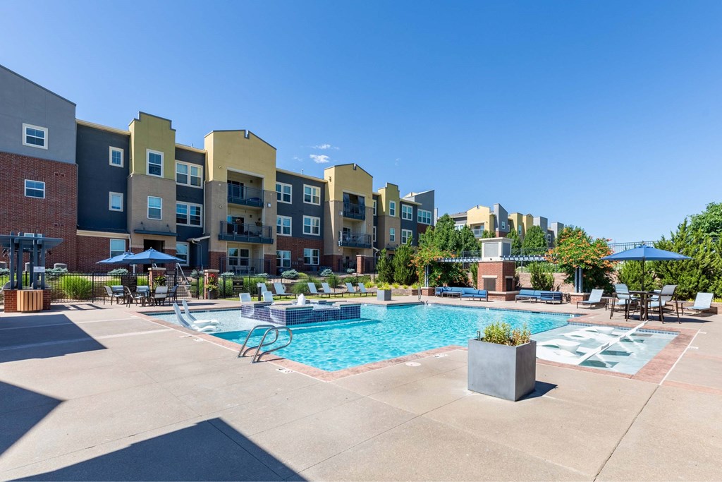 A swimming pool surrounded by chairs and umbrellas in front of apartment buildings.