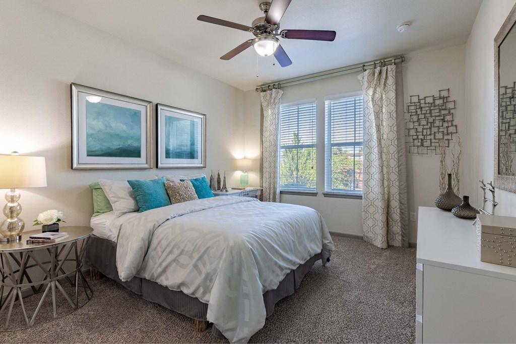 A bedroom with a bed, a ceiling fan, and two wall lamps.