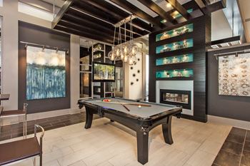 A pool table is in the middle of a room with a fireplace and a painting on the wall.