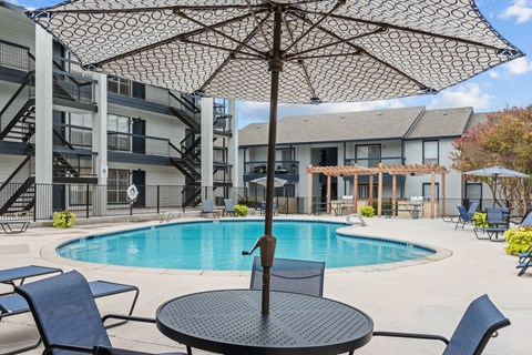 A black umbrella is over a table in the middle of a pool.