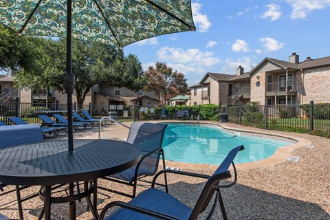 A patio with a table, chairs and an umbrella overlooking a pool.