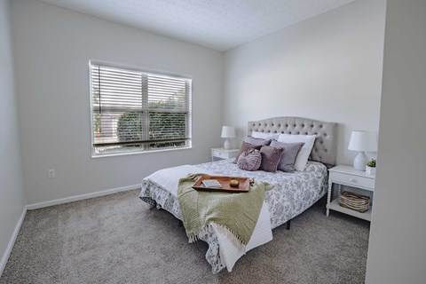 A bedroom with a large bed and a window with blinds.