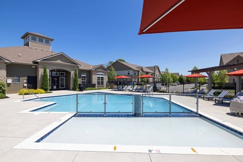 A large swimming pool in front of a building with a red umbrella.