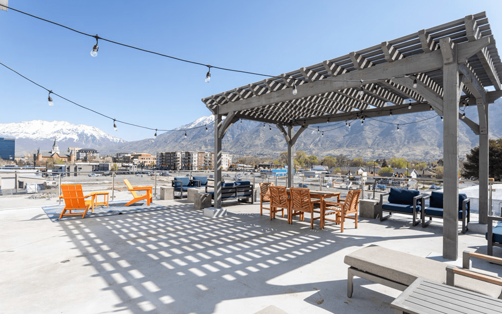 A patio with a pergola and chairs overlooking a snowy mountain range.
