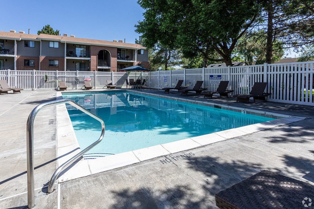 A pool surrounded by a white fence and chairs.