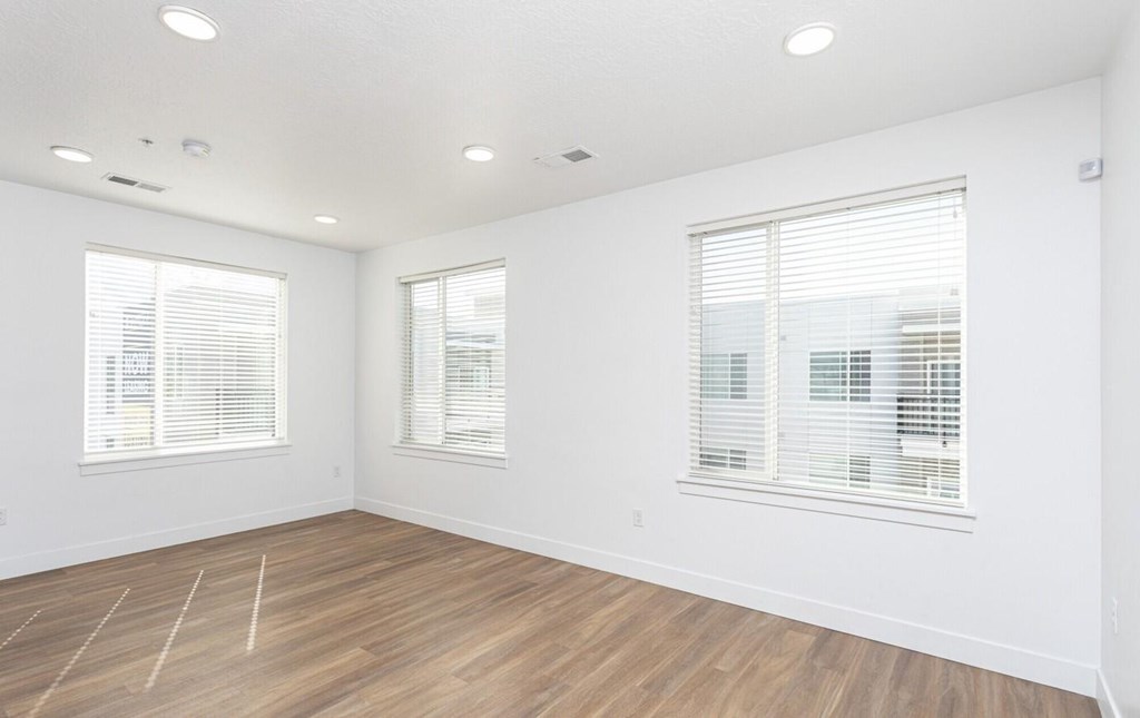 A room with wooden flooring and two windows with blinds.