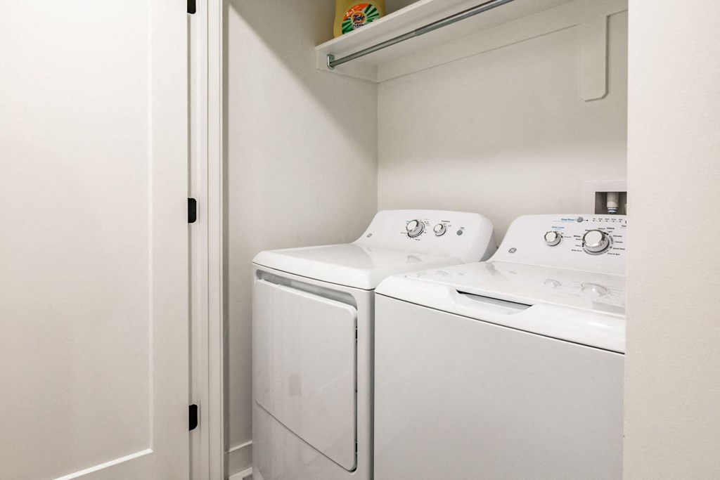 a washer and dryer in a white laundry room with a shelf above it