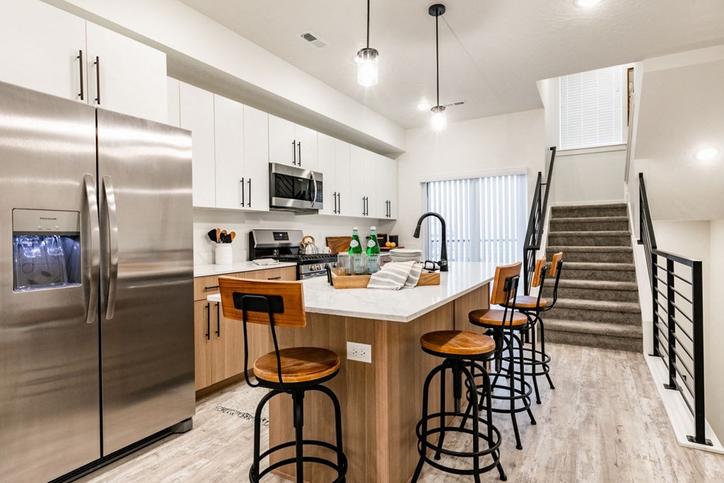 a kitchen with a counter with bar stools and a stainless steel refrigerator