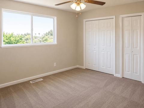 A room with a carpeted floor, two doors, and a window with a view of trees.