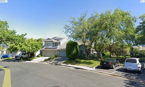 A street view of a residential area with houses and parked cars.
