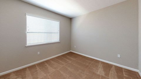 A room with a carpeted floor and a window with blinds.