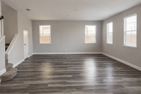 A spacious room with wooden flooring and three windows.