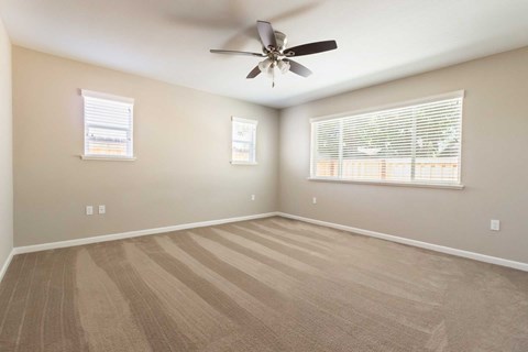 A room with a ceiling fan and two windows.