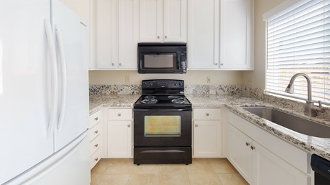 A black stove and microwave in a kitchen with white cabinets.