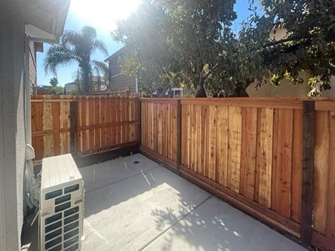 A wooden fence and a white air conditioning unit are on a patio.