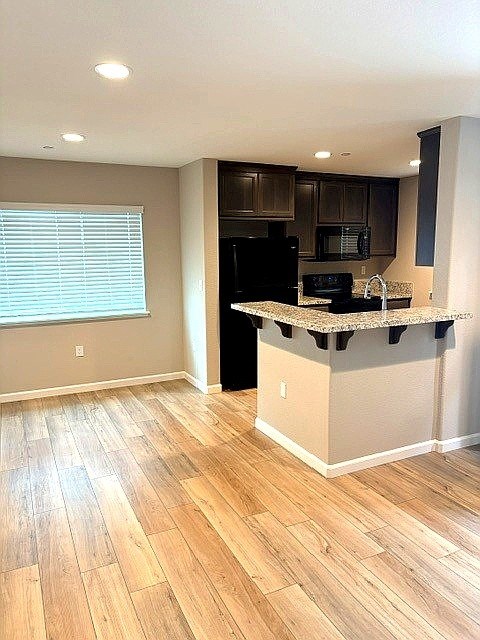 A kitchen with a black refrigerator and wooden floors.