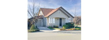 A house with a grey facade and a red roof is surrounded by a well-maintained lawn and a clear sky.