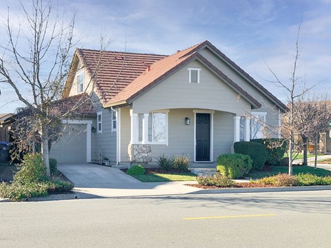 A house with a grey facade and a red roof is surrounded by a well-maintained lawn and a clear sky.