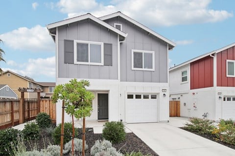 A modern house with a grey and white exterior and a red and white house in the background.
