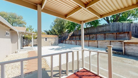 A patio with a white railing and a red mat on the floor.