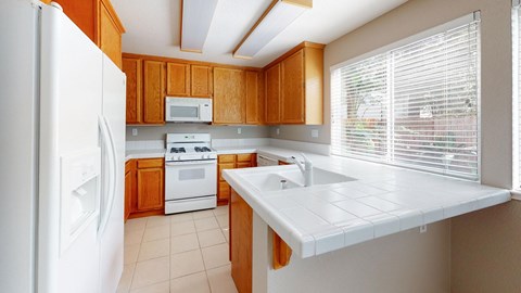 A kitchen with a white refrigerator, white countertop, and wooden cabinets.