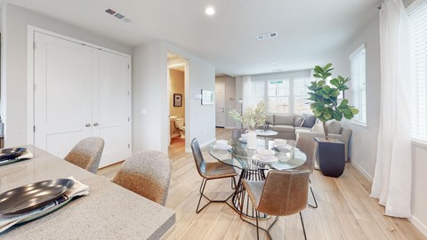 A dining room with a table set for two and a potted plant on the side table.