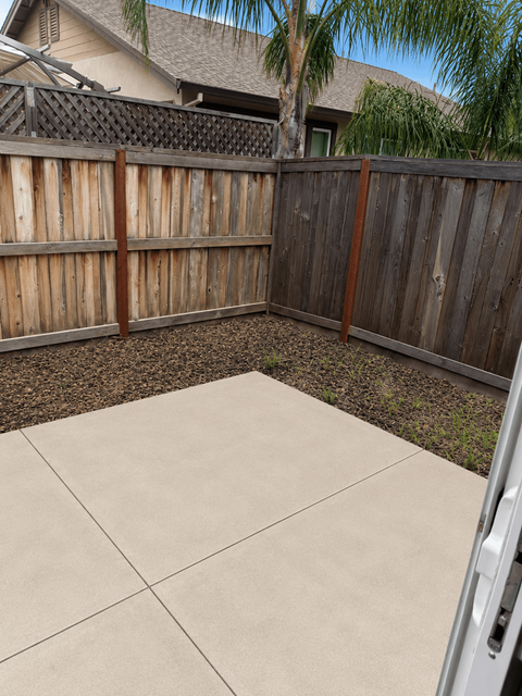 A backyard with a wooden fence and a concrete patio.