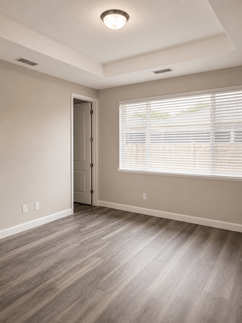 A room with a wooden floor and a door leading to another room.