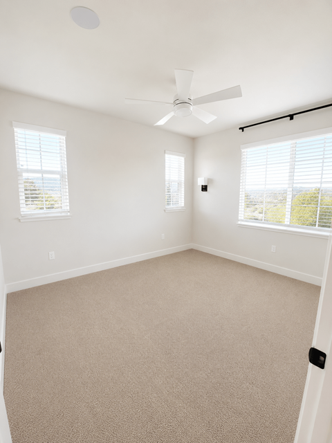 A room with a carpet floor, a ceiling fan, and two windows.