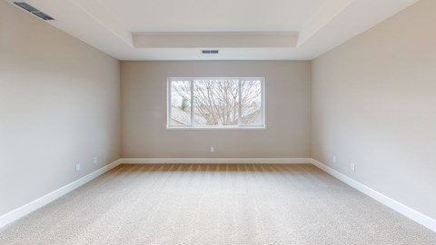 A large empty room with a window and carpeted floor.