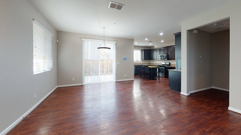 A spacious room with wooden floors and a kitchen area in the background.