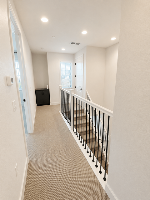 A hallway with a carpeted floor and a black railing.