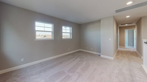 A spacious room with carpeted flooring and two windows.