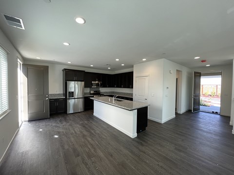 A spacious kitchen with dark wood flooring and white walls.